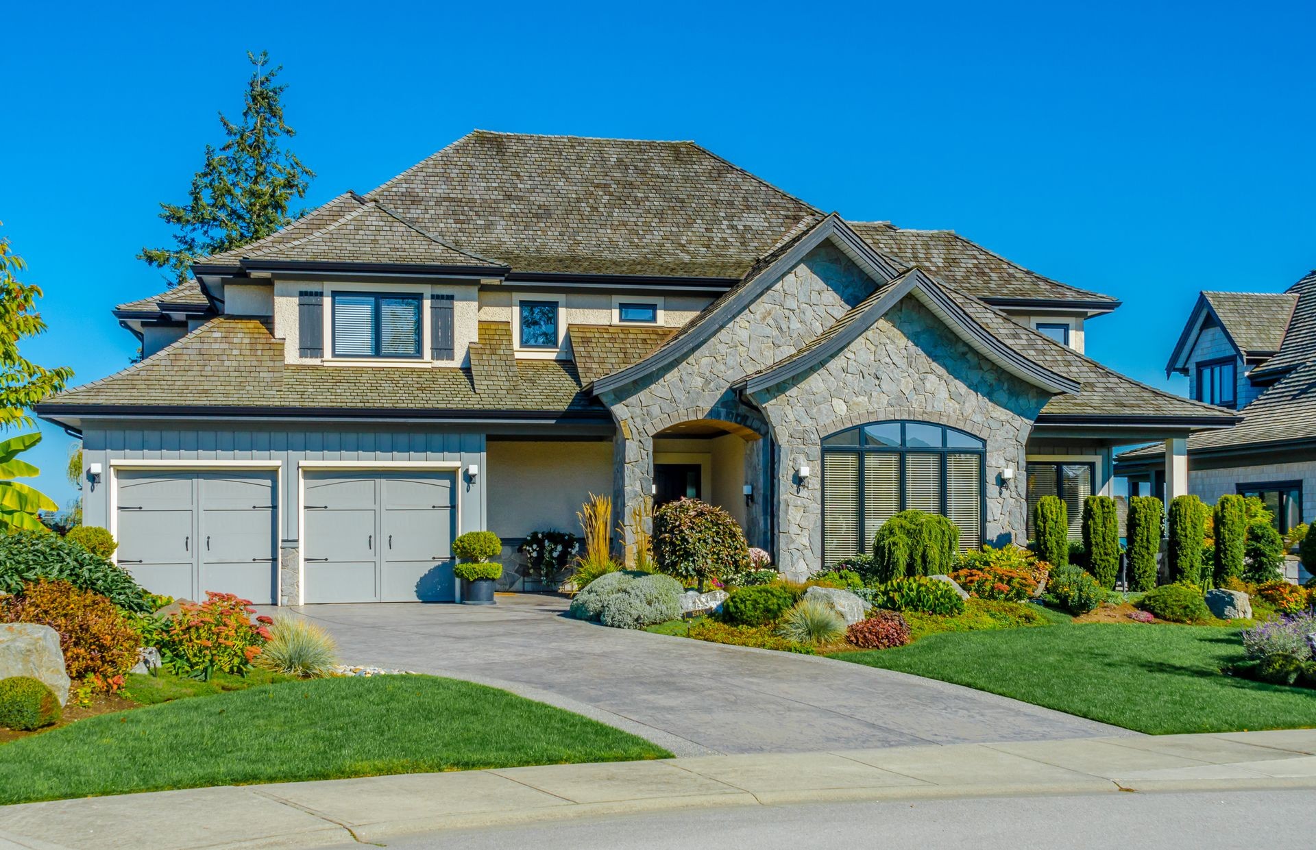 Big custom made luxury house with nicely landscaped and trimmed front yard and driveway to garage in the suburbs of Vancouver, Canada.