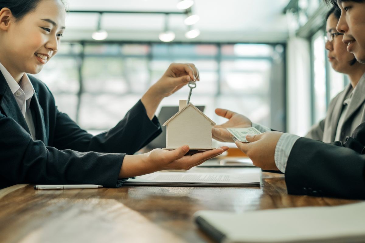 Real estate agents holding model house and keys for submit documents for customers to sign for a sale contract,real estate concept.